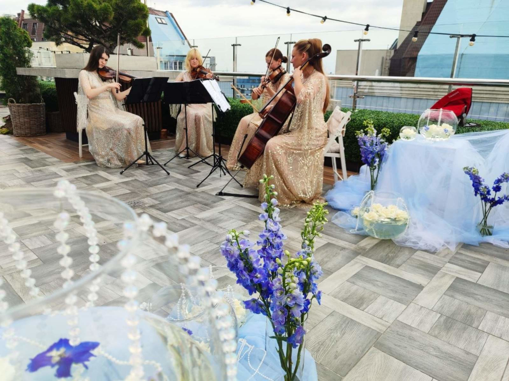 Струнний квартет NAVA виконує романтичні композиції на весільному open air заході на даху сучасного комплексу в елегантних золотих сукнях.